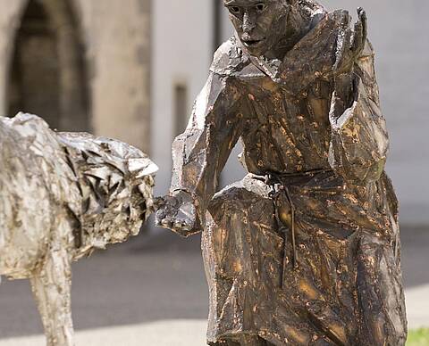 Bronzestatue eines knienden Mannes, der einem Wolf die Hand reicht